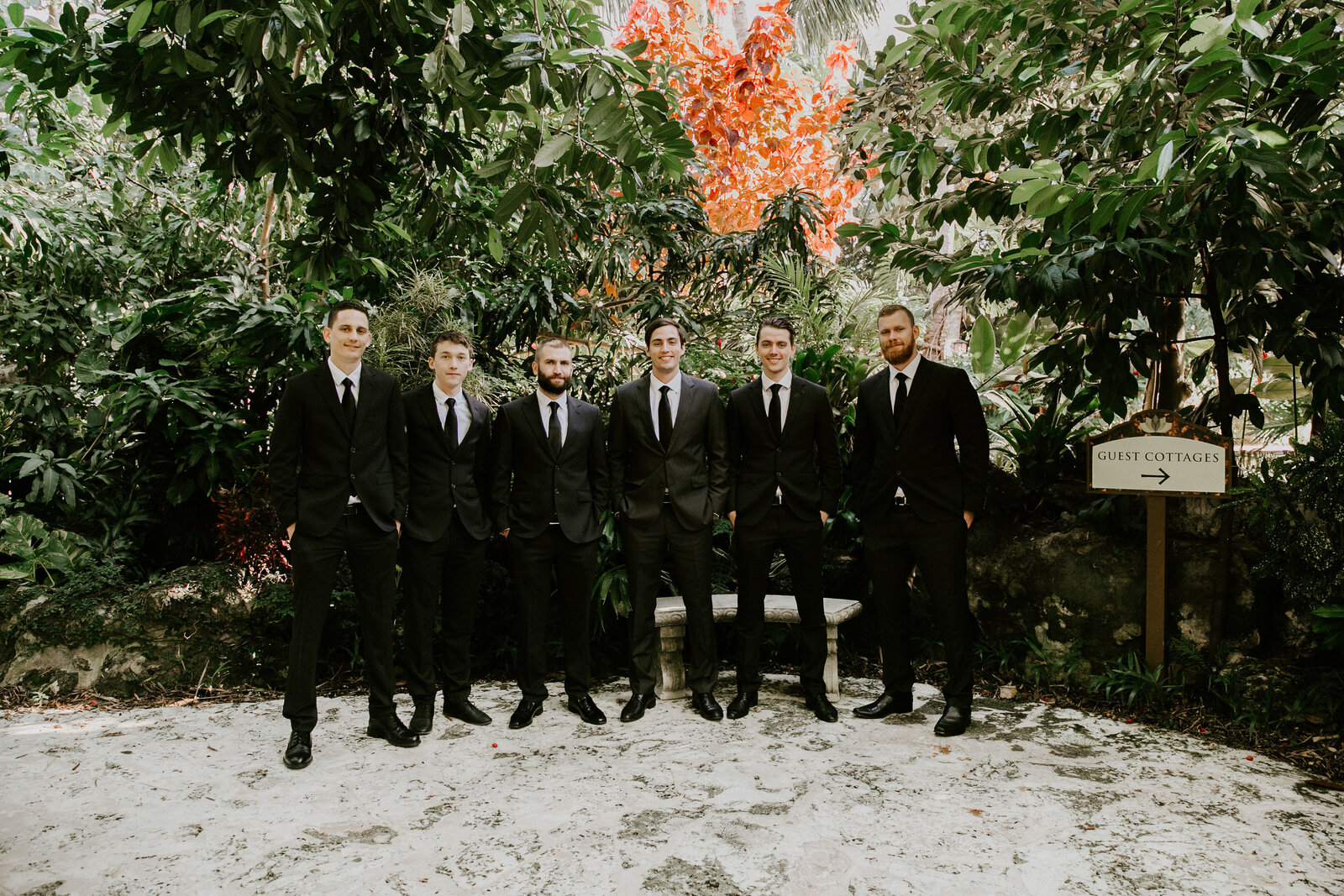 Groomsmen in black tie walking a shaded garden path